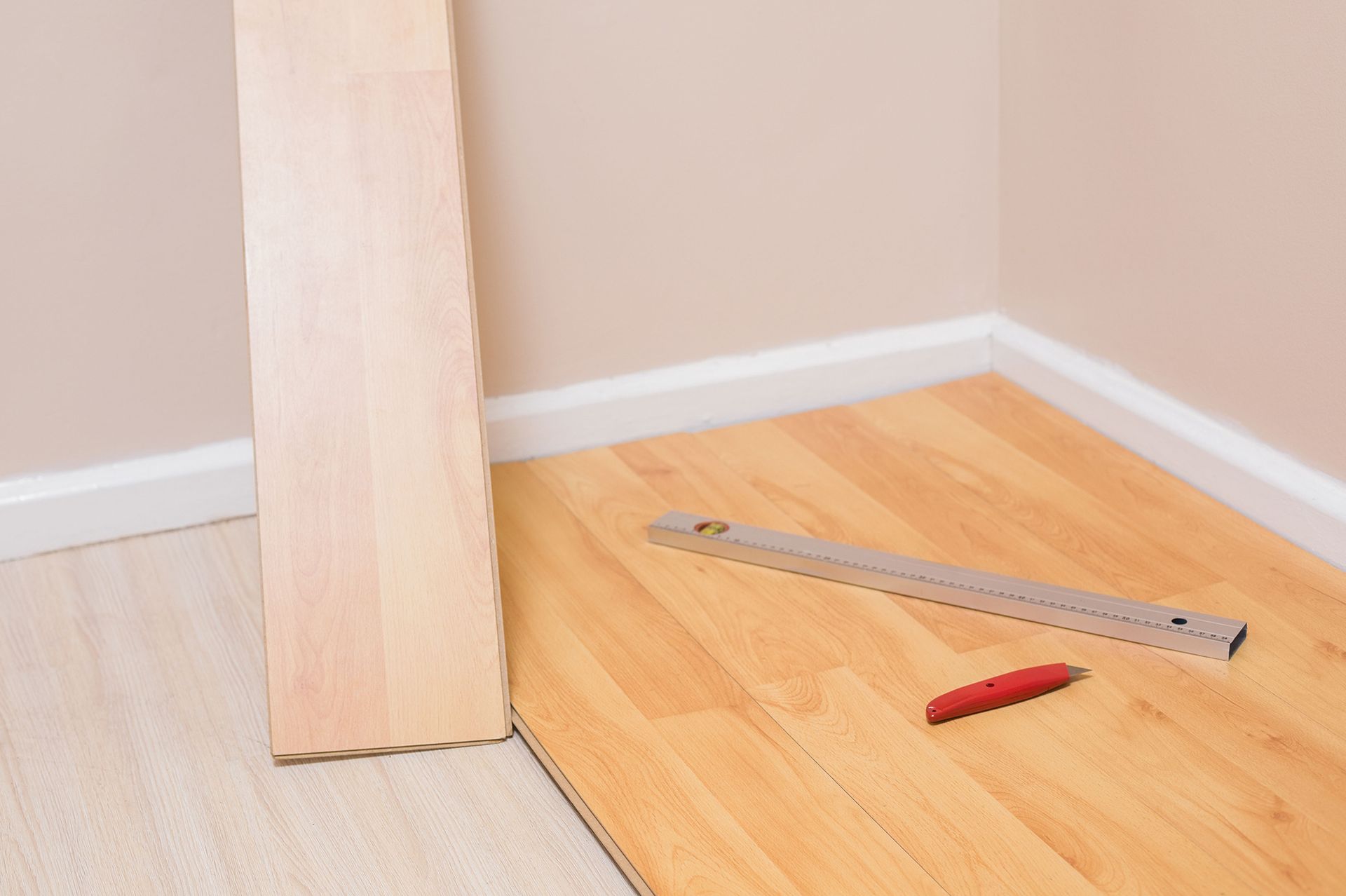 Flooring tools on a hardwood floor beside a wall panel and ruler.