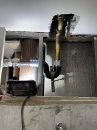 Open ceiling with exposed plumbing pipe and black drain fitting above a tiled bathroom wall