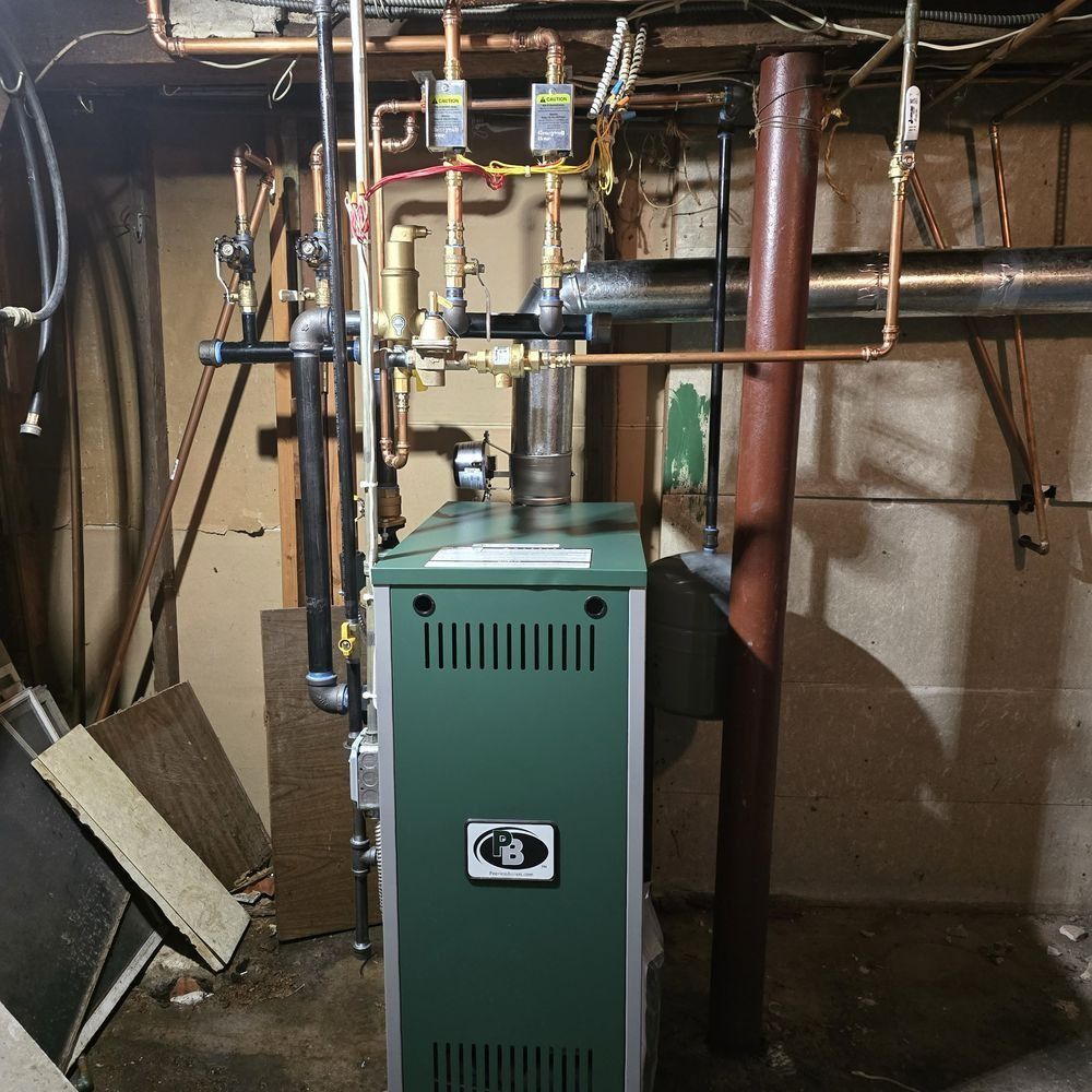 Green furnace and exposed pipes in a basement utility room.