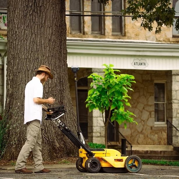 Man mowing lawn with a yellow mower beside a tree and building
