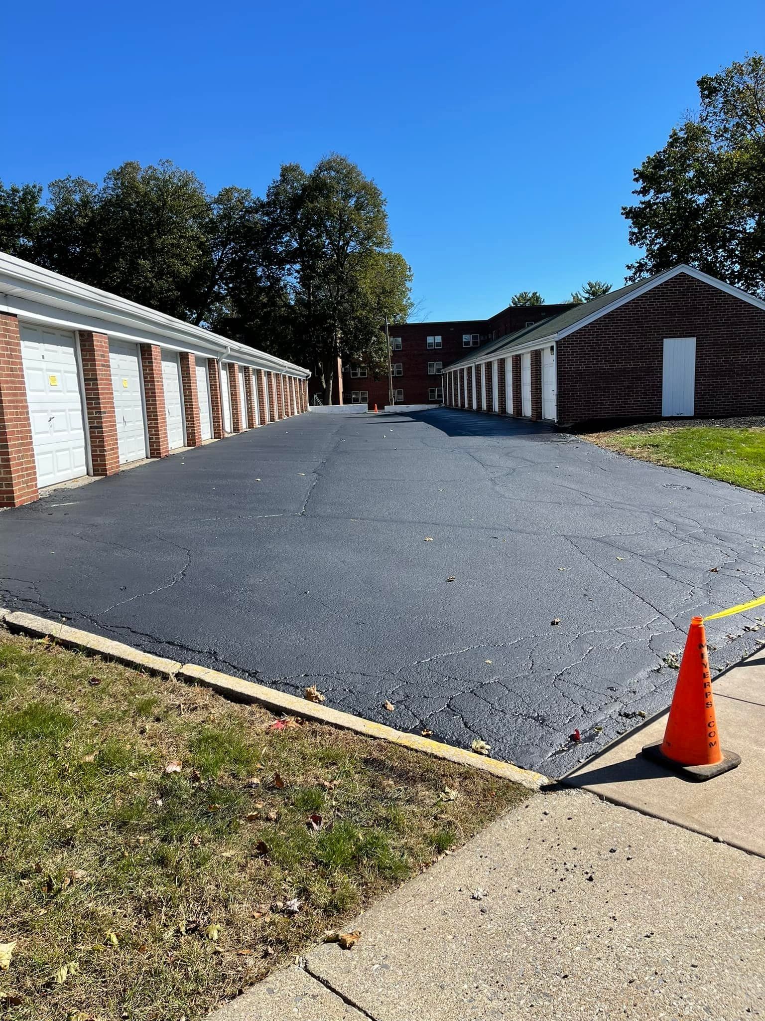 Gravel driveway between white brick garages under a blue sky, with an orange cone in the foreground.
