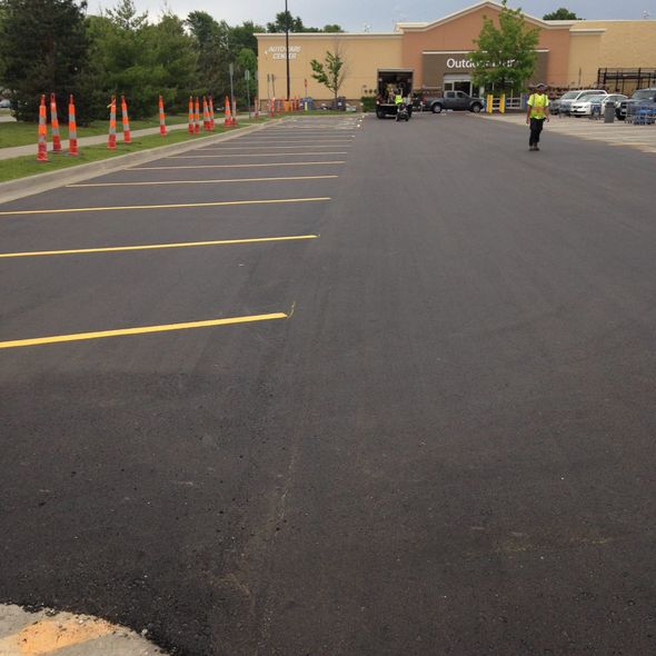 Newly paved asphalt parking lot with yellow parking space lines. Cones line the edge.
