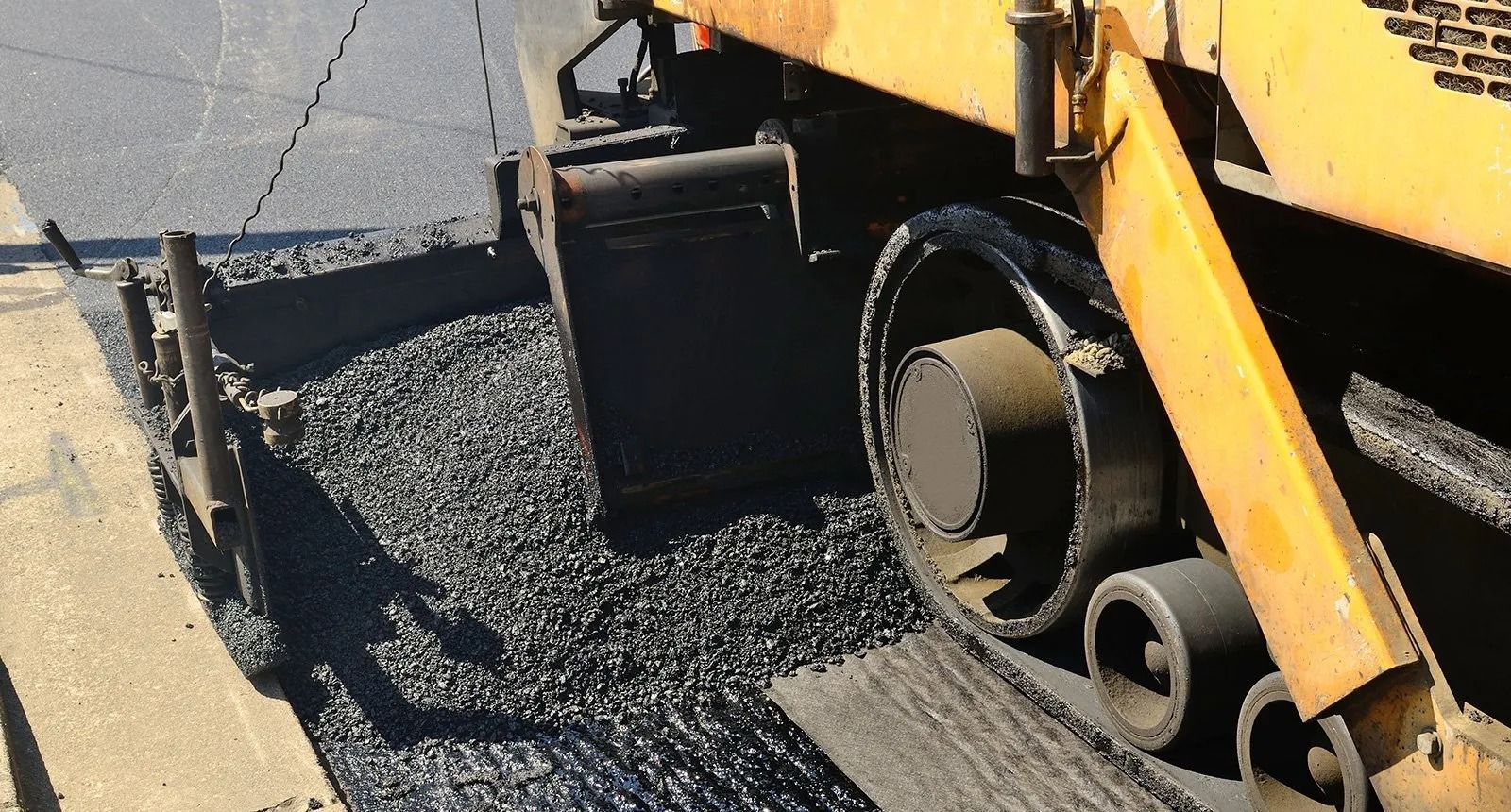 Asphalt paving machine laying fresh black asphalt on a road.