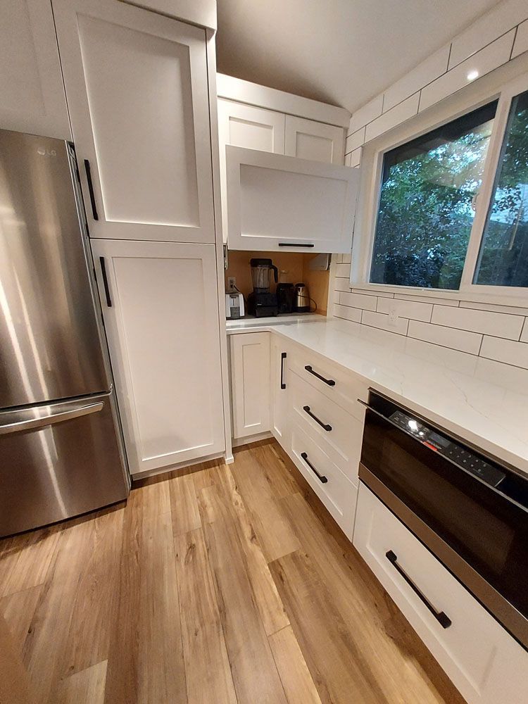 A kitchen with white cabinets,  stainless steel appliances, and a large window