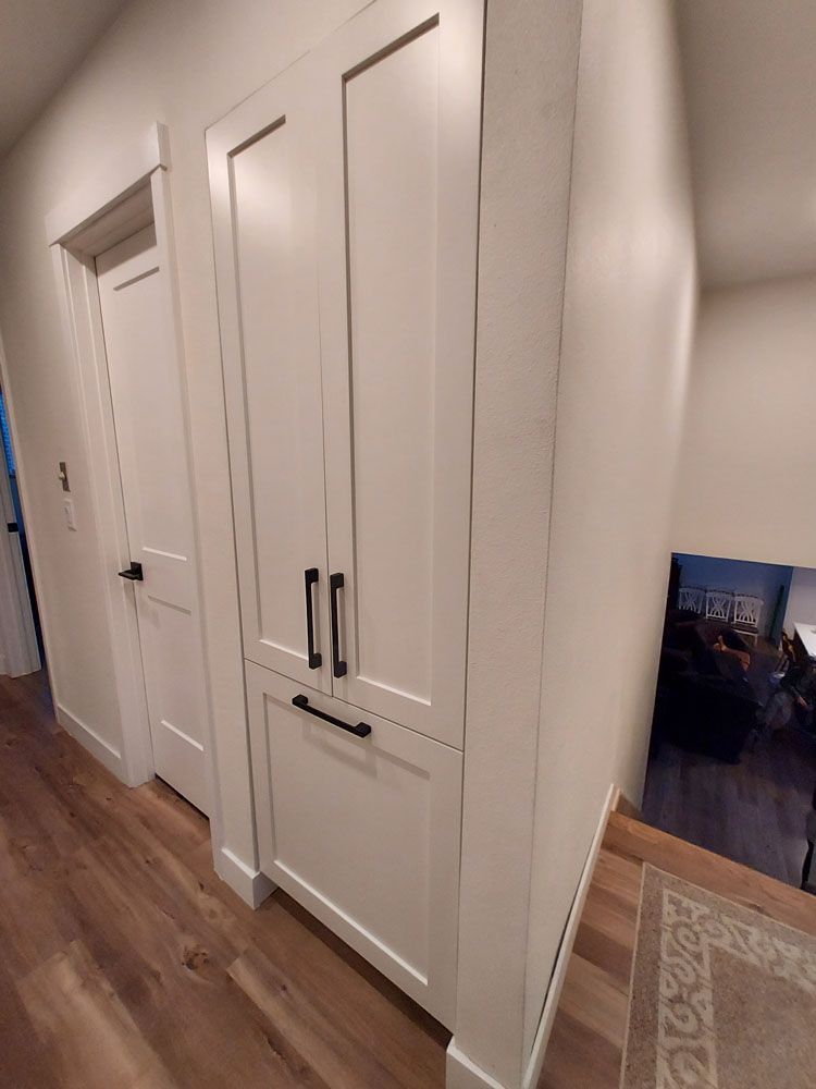 A white cabinet with black handles is in a hallway next to a door