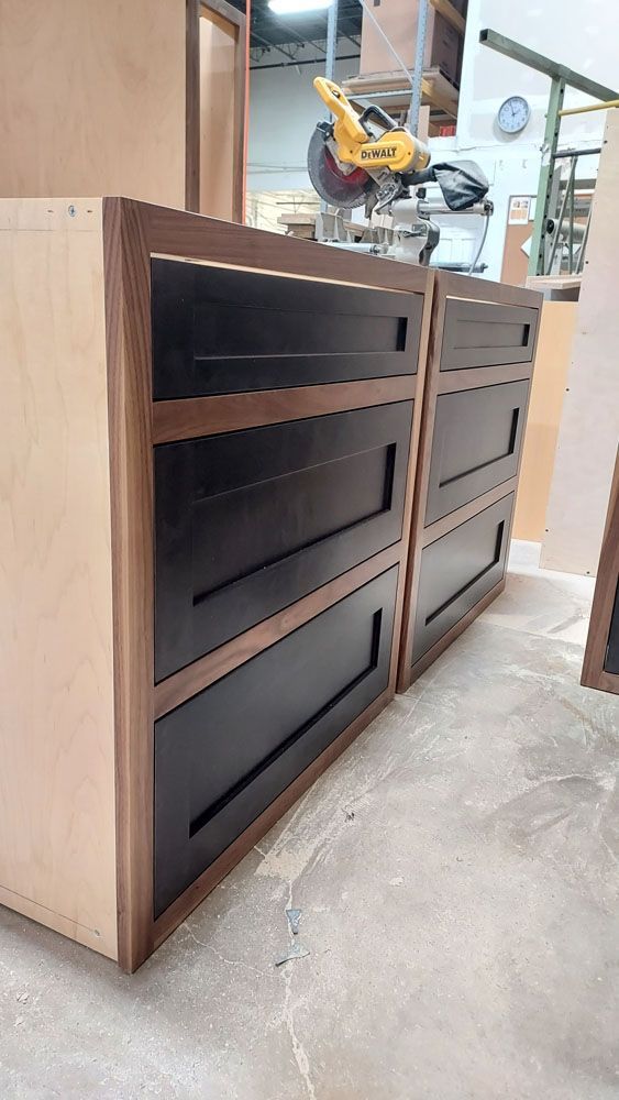 A wooden dresser with black drawers is being built in a workshop