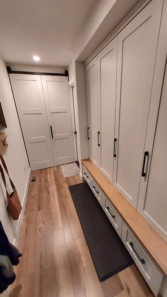 A hallway with white cabinets and wooden floors leading to a door