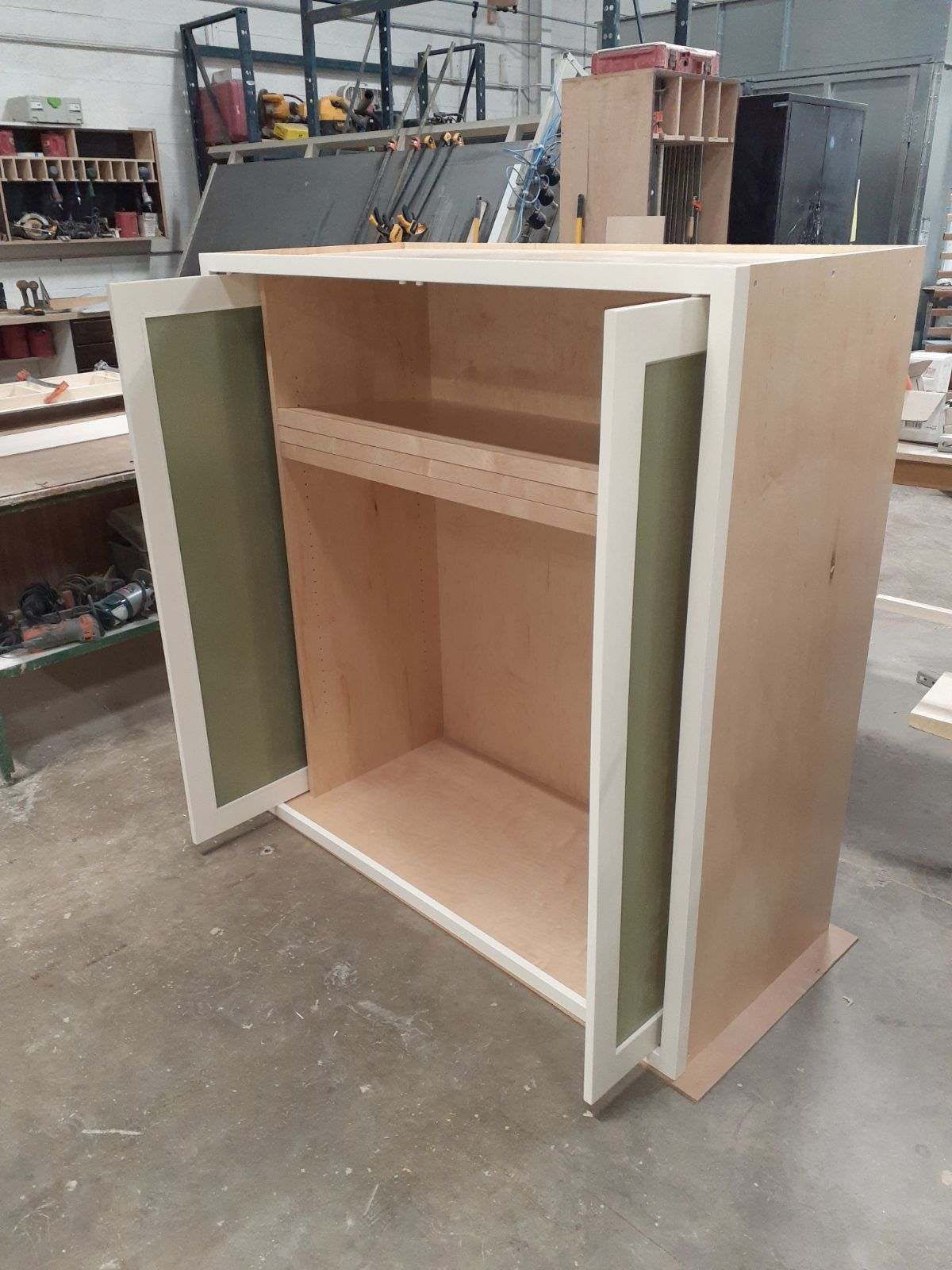 A wooden cabinet is being built in a workshop with the doors open