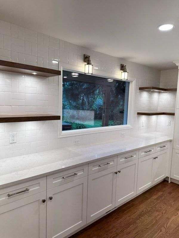A kitchen with white cabinets, white countertops, and a window