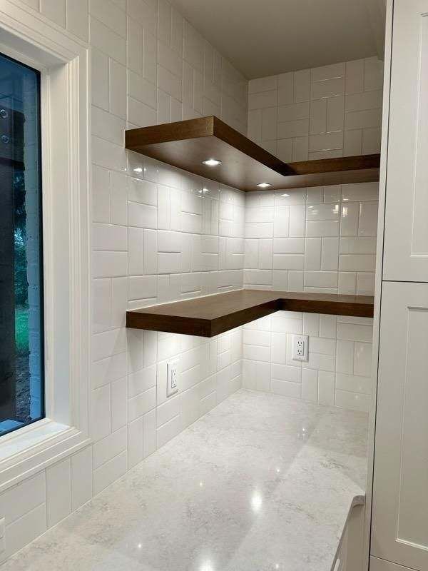 A kitchen with white tiles wooden shelves and a window