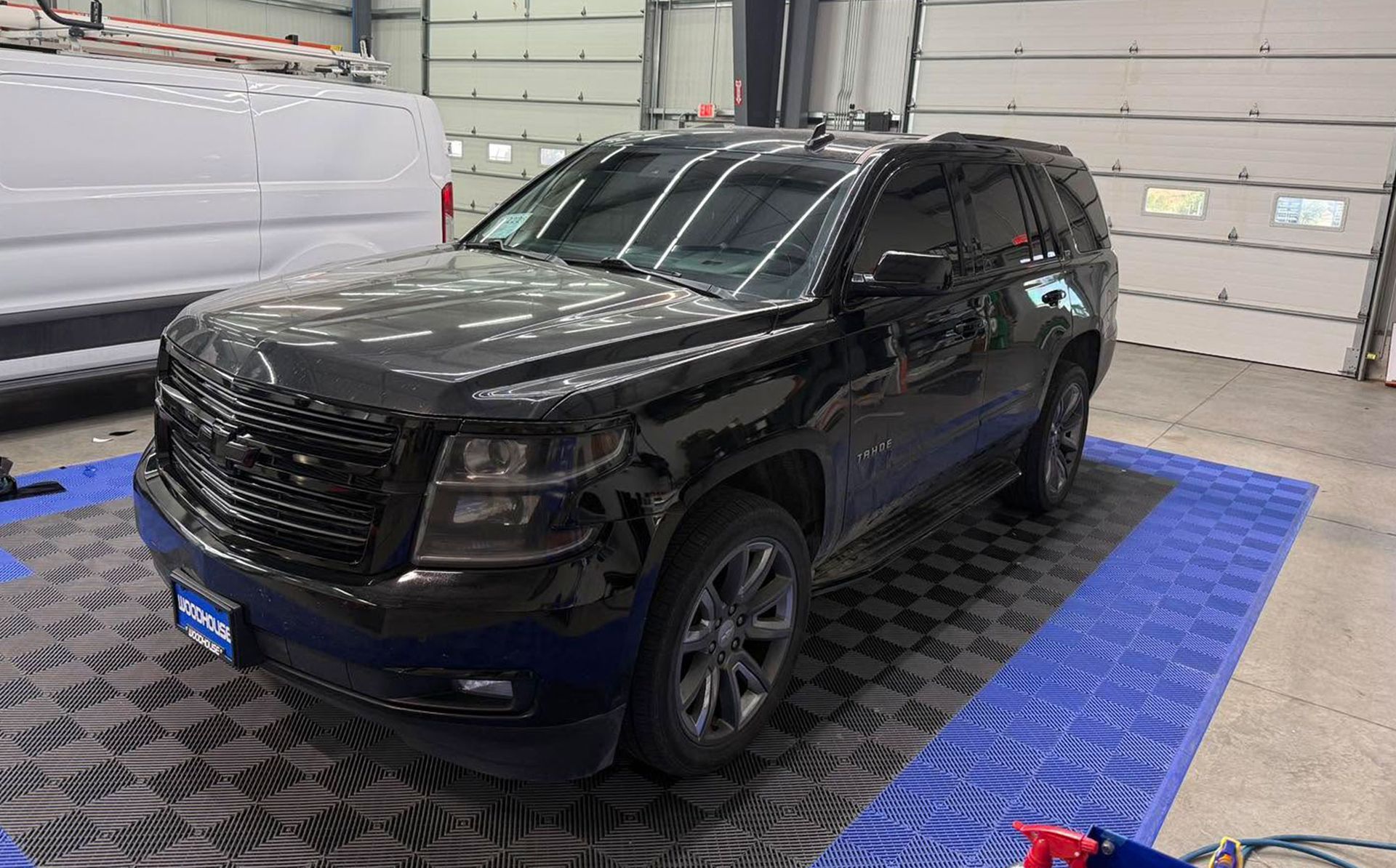 Black SUV parked indoors on a blue textured mat in a garage, front-left view.