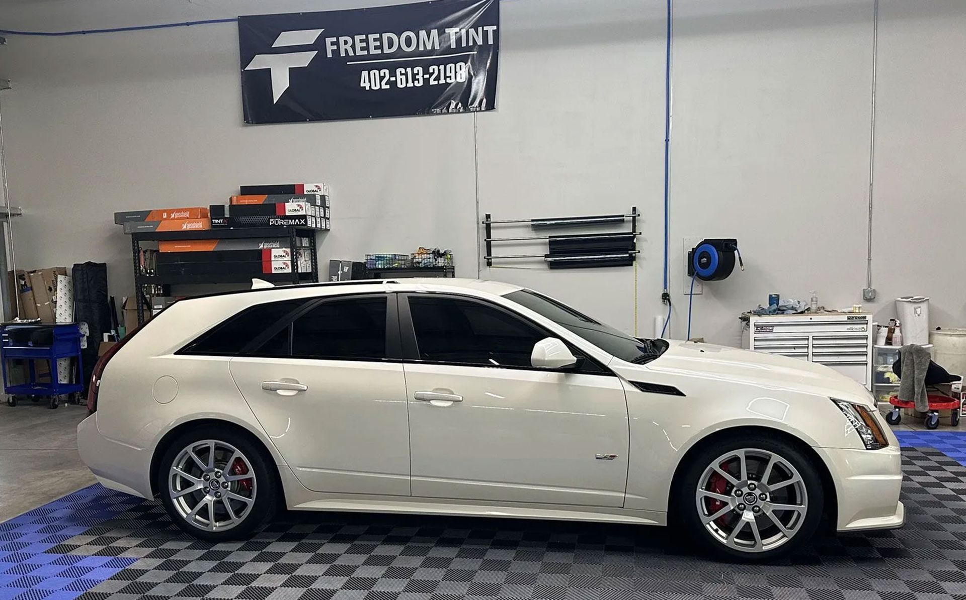 White sports sedan in an auto shop garage with tools and a Freedom Ink banner on the wall