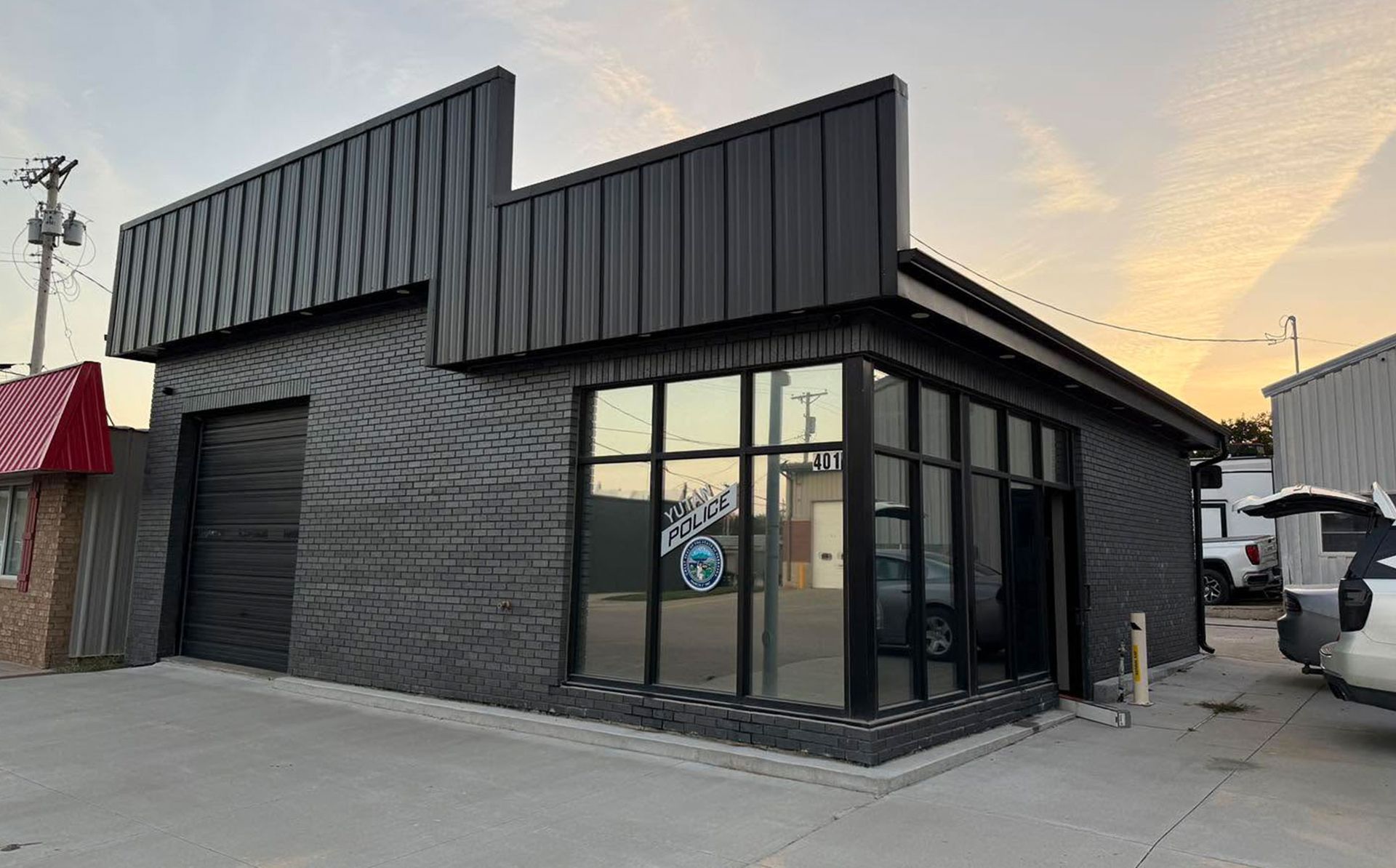 Black modern storefront with corrugated metal facade and large glass windows at sunset