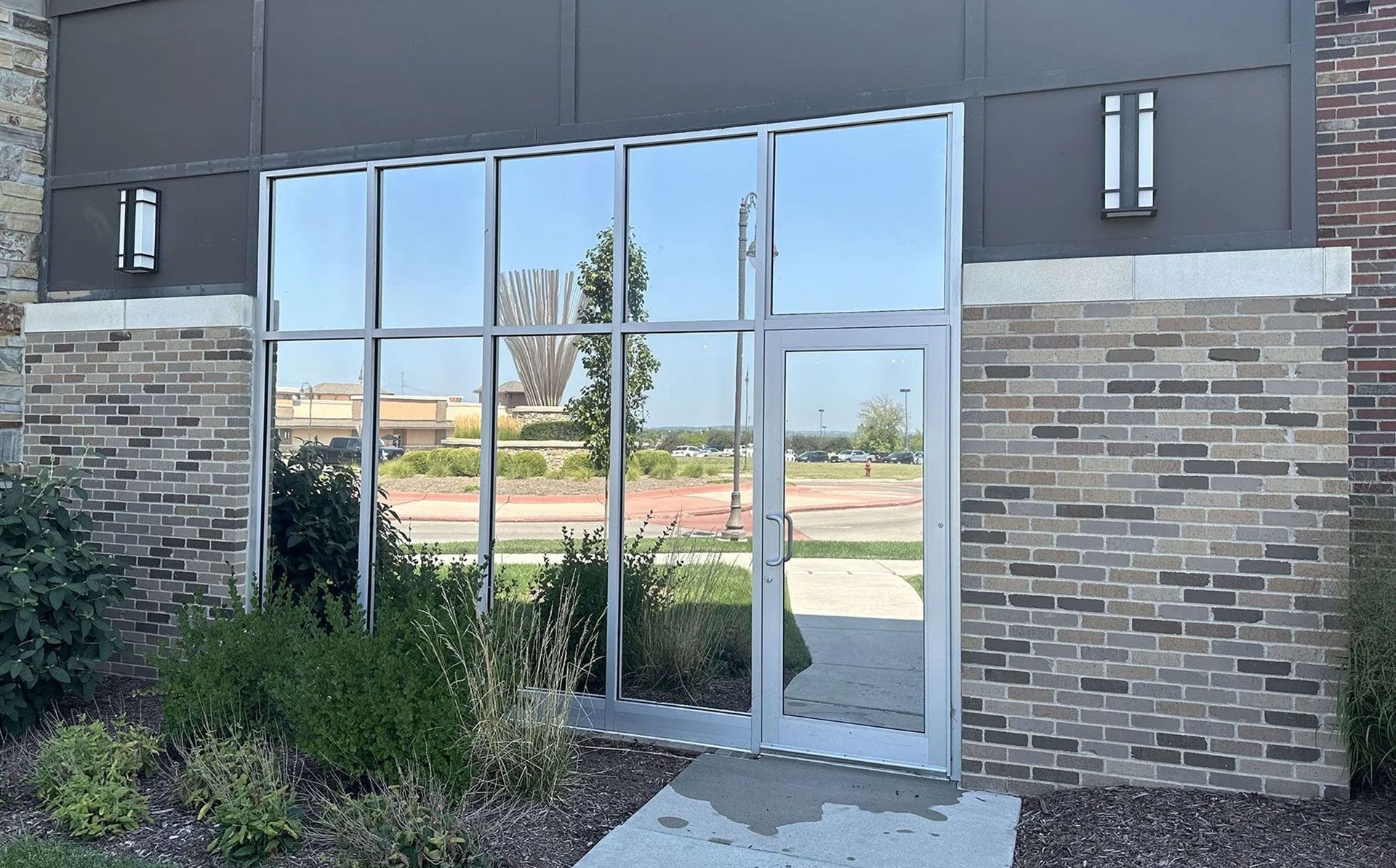 Modern building entrance with glass double doors, stone walls, and landscaped shrubs.