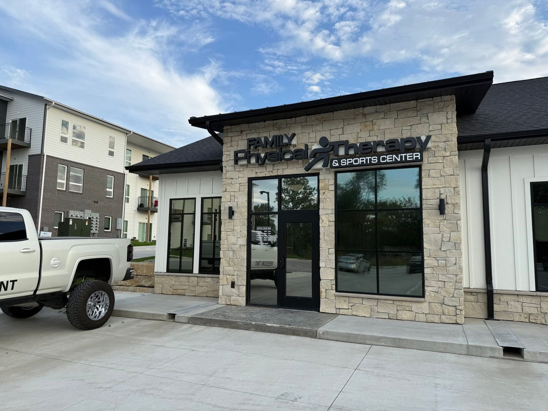 Front of a stone storefront with glass doors and windows, next to a white truck in a parking lot.