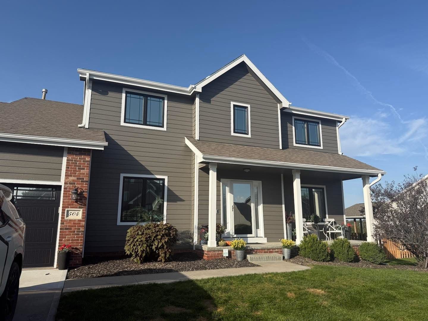 Two-story gray house with white trim, front porch, and brick garage under a clear blue sky