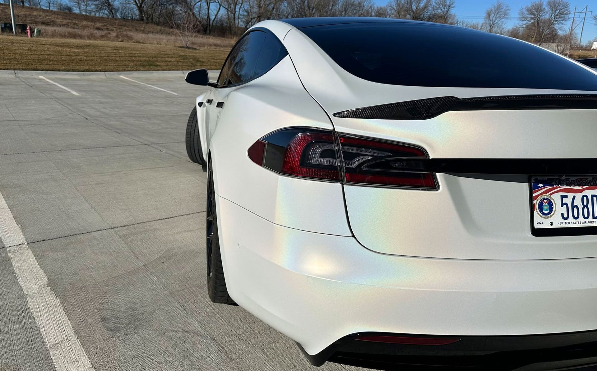 White sports sedan parked on a concrete lot, rear view with tinted windows and visible license plate.