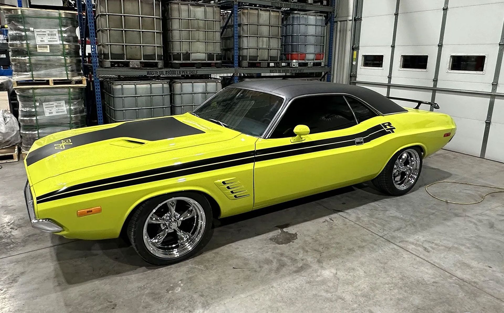Yellow classic muscle car with black racing stripes parked in a warehouse garage