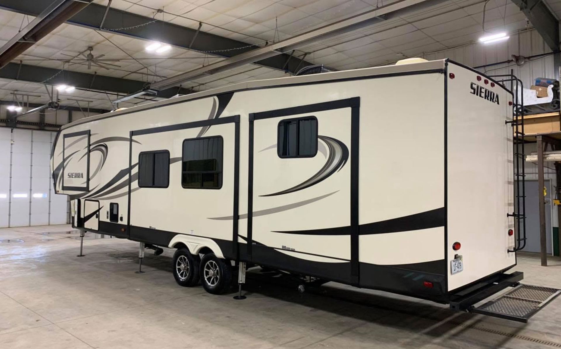 Large white fifth-wheel RV trailer with black swirl graphics parked indoors under warehouse lights.