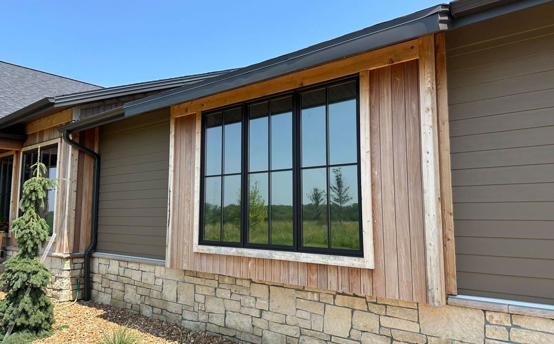 Exterior of a modern house with large black-framed windows, wood trim, and stone base siding