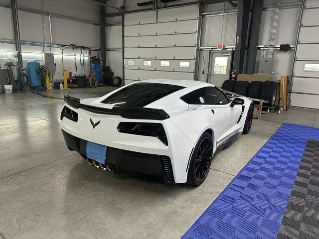 White sports car in an industrial garage, rear view on a concrete floor beside a blue mat