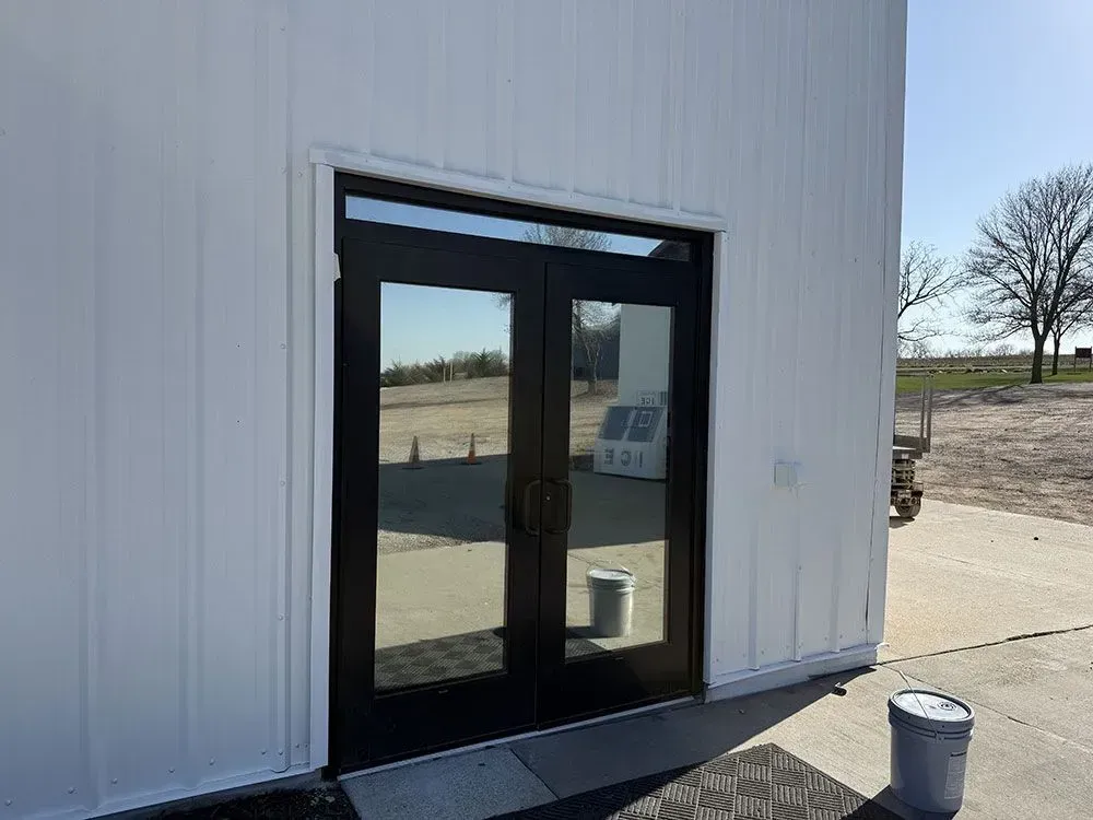 Black double glass doors on a white building exterior with a concrete walkway and open field beyond