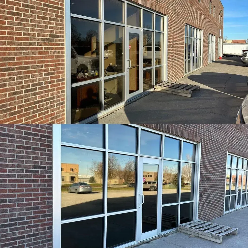 Brick commercial building with large glass windows and doors along a sidewalk.