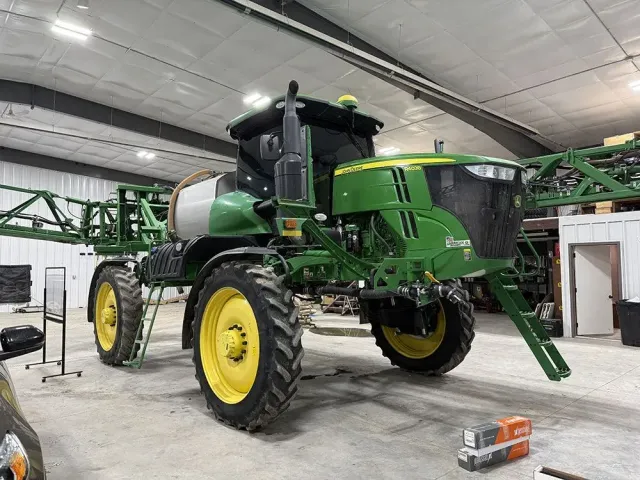 Green John Deere tractor inside a warehouse, with yellow wheels and a large front tank attachment