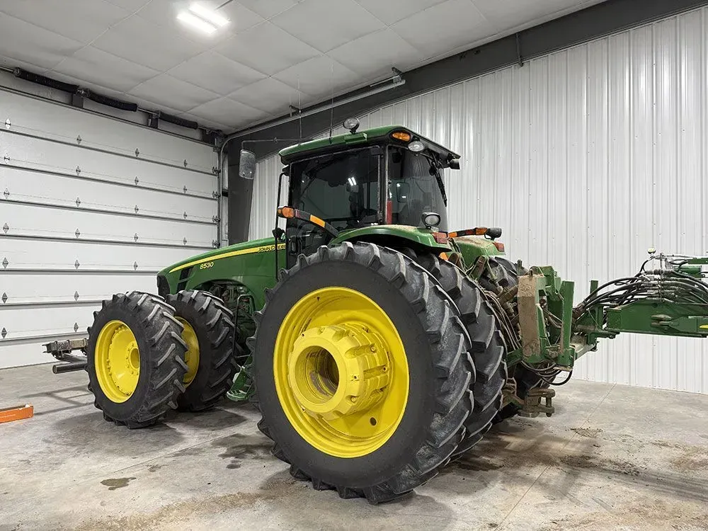 Green tractor with large yellow wheels parked inside a white garage or workshop.