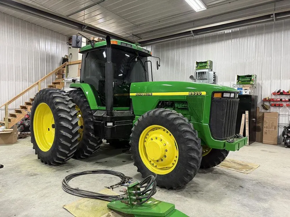 Green John Deere tractor inside a workshop, with yellow wheels and a coiled hose on the floor.