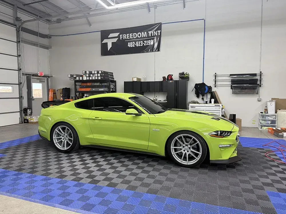 Lime green sports coupe parked in an auto shop with a checkered floor and tools in the background