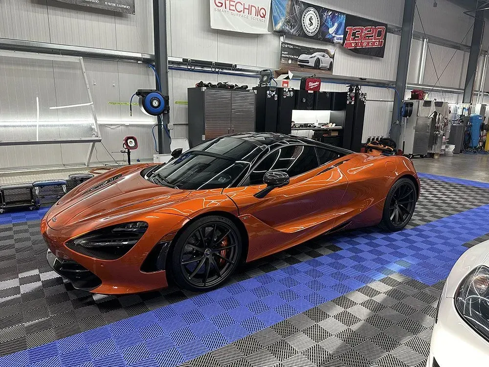Orange McLaren sports car on a blue and gray checkered floor inside a workshop.