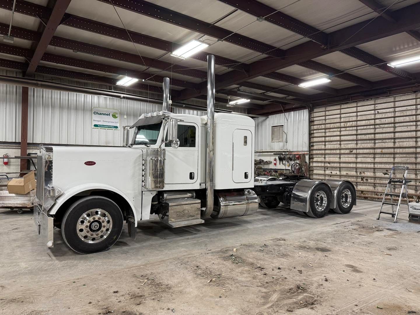 White semi-truck parked inside a metal garage with high ceiling lights