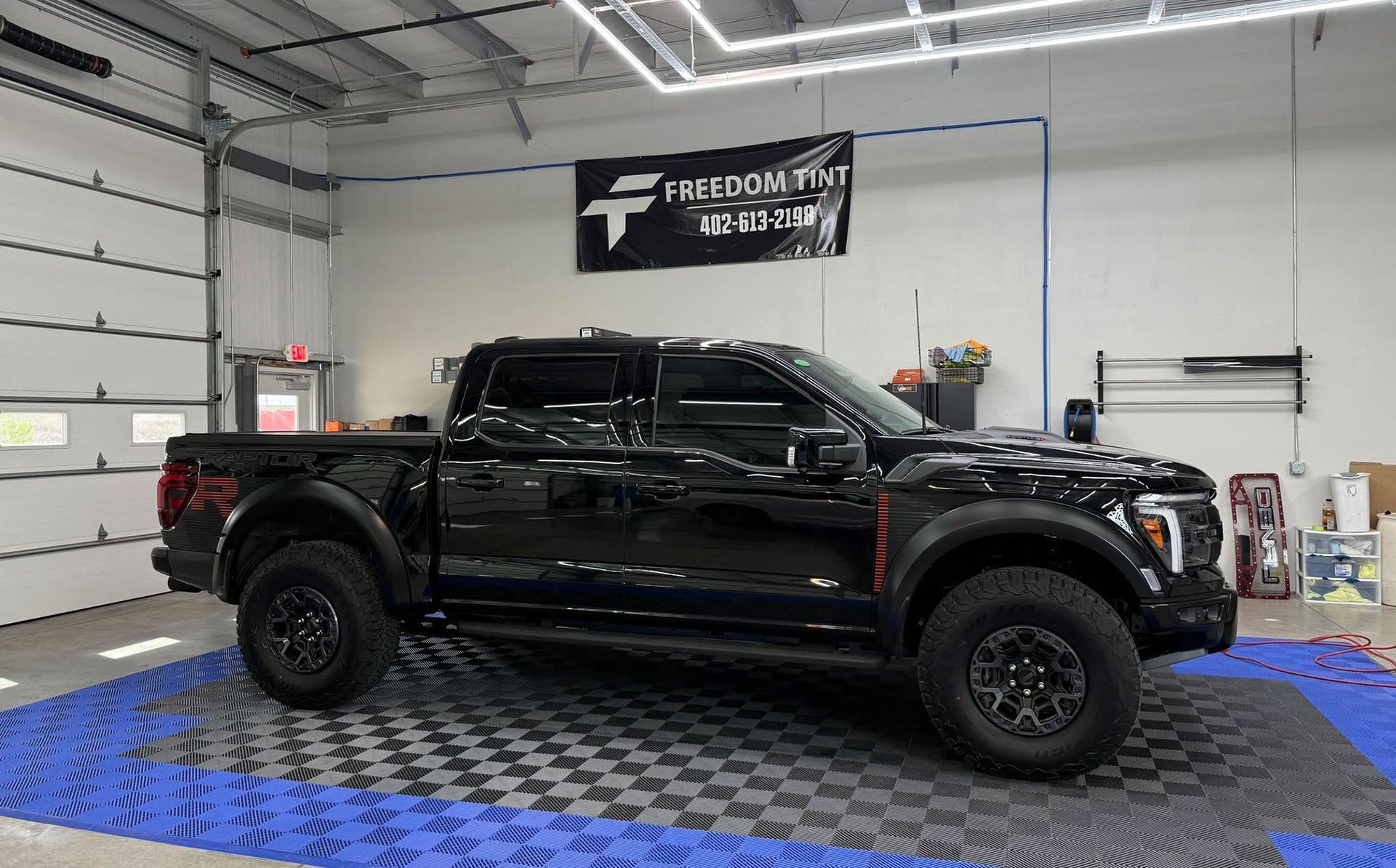Black lifted pickup truck in a workshop with a blue checkered floor and Freedom logo on the wall