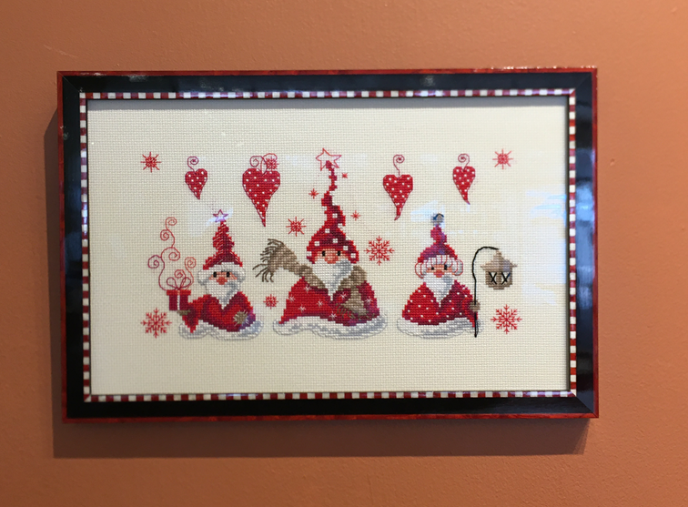 A cross stitch of santa clauses and snowmen is hanging on a wall