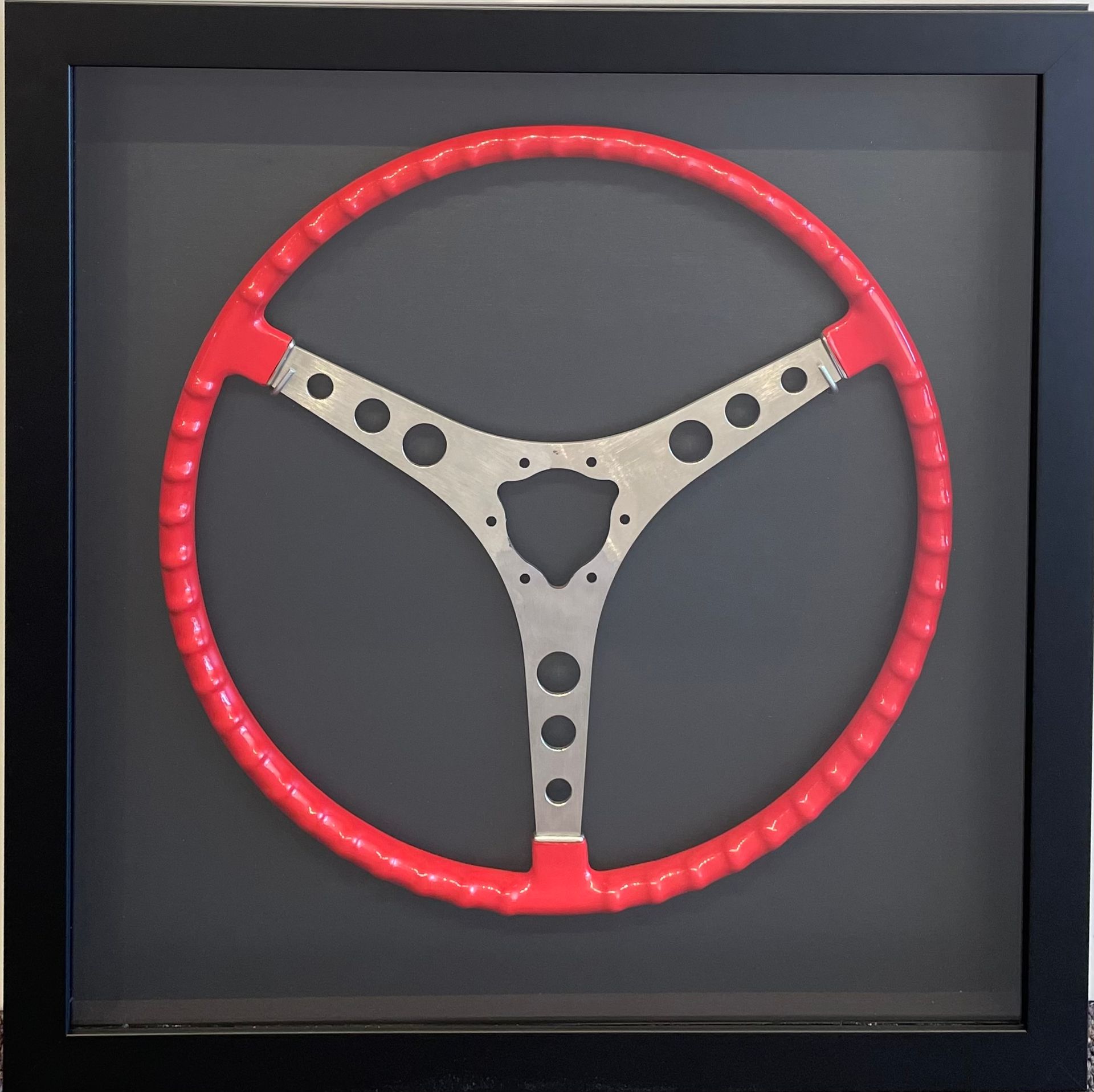 A red and silver steering wheel in a black frame