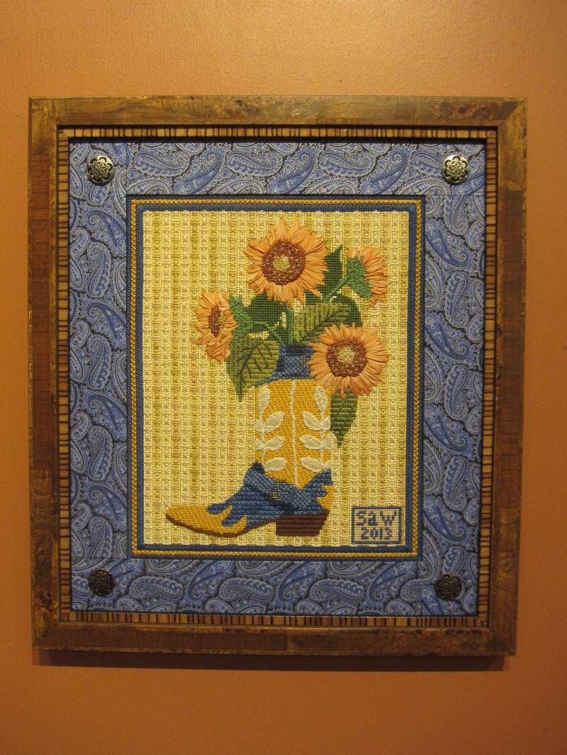 A picture of a vase of sunflowers and cowboy boots in a frame on a wall.