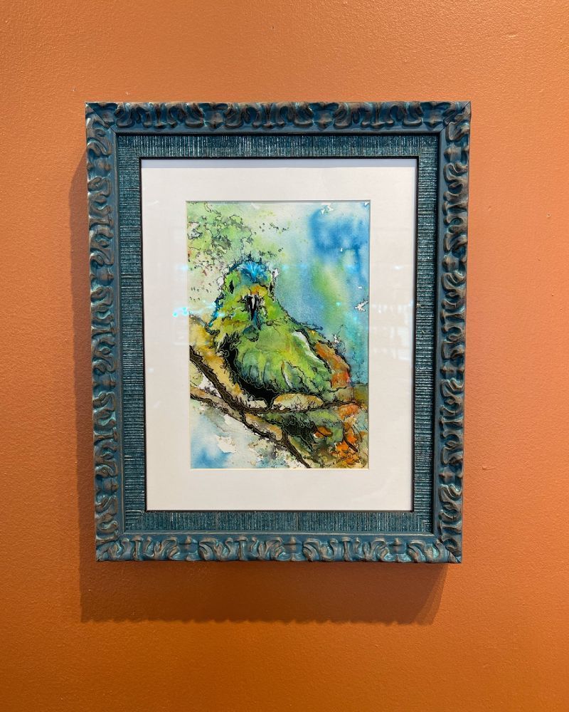 A painting of a bird in a blue frame is hanging on a wall.