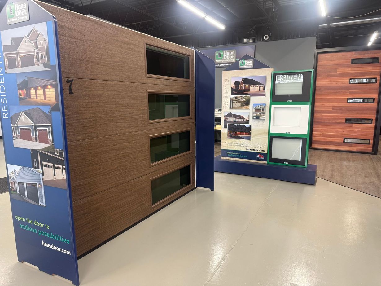 A showroom display of various garage door panels with window inserts and wood-grain finishes in a retail store.
