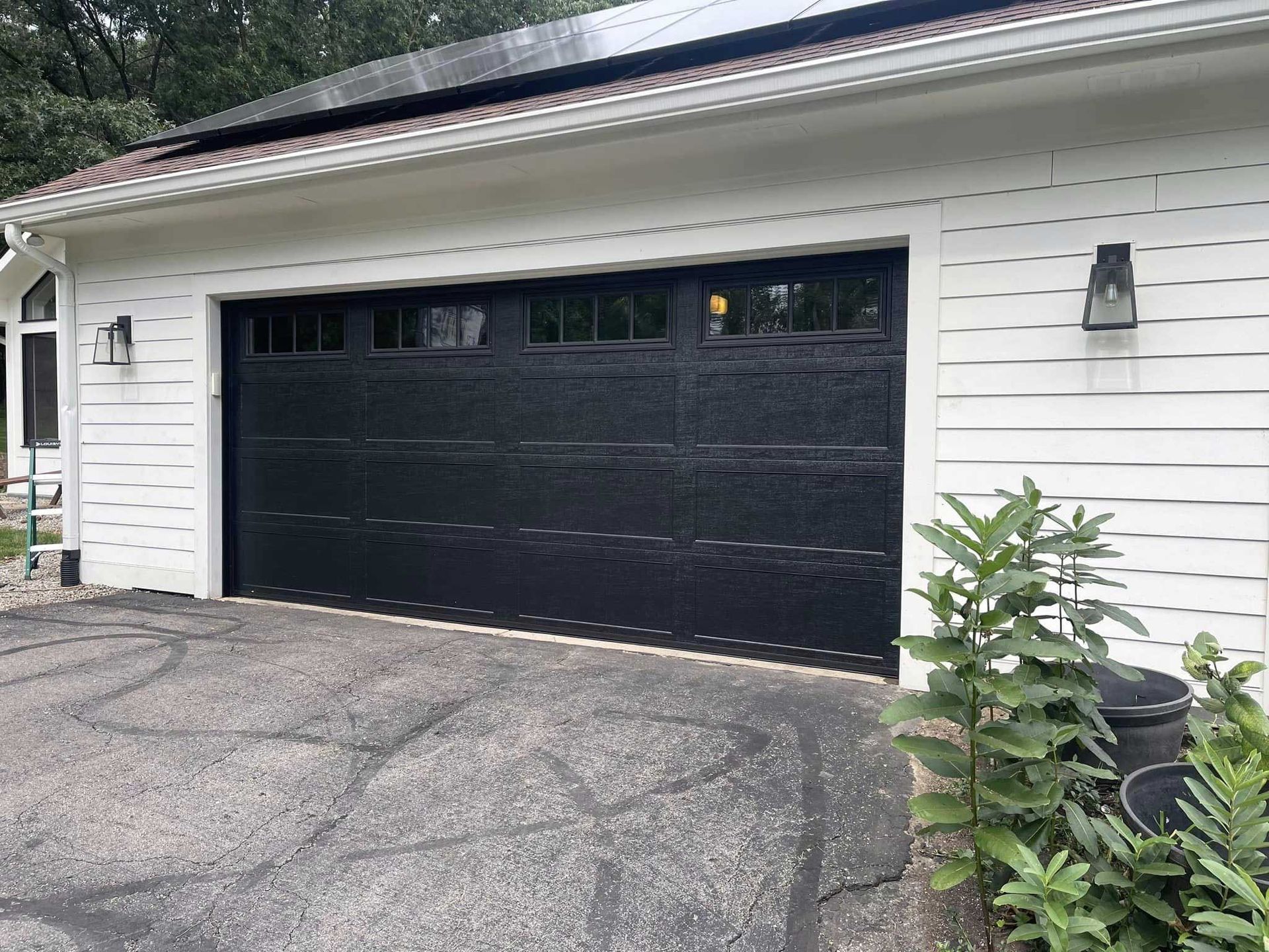Black garage door on a white house, with solar panels on the roof and a dark paved driveway.