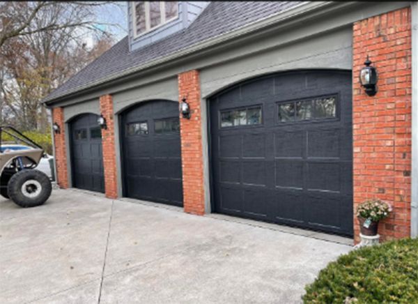 Three black garage doors with arched tops; brick columns and gray trim.