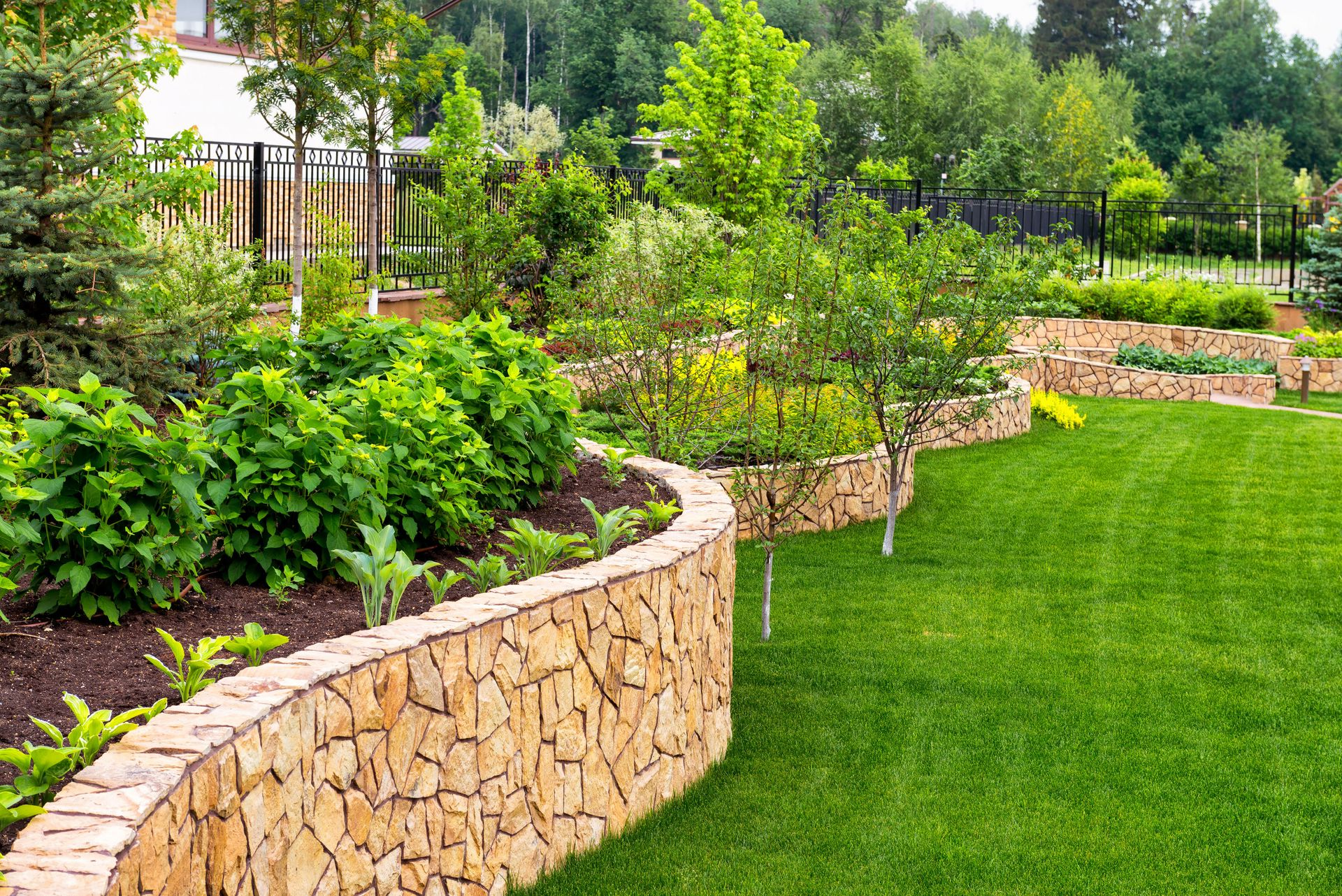 Curved stone garden wall bordering a lush green lawn and landscaped shrubs in a park-like yard