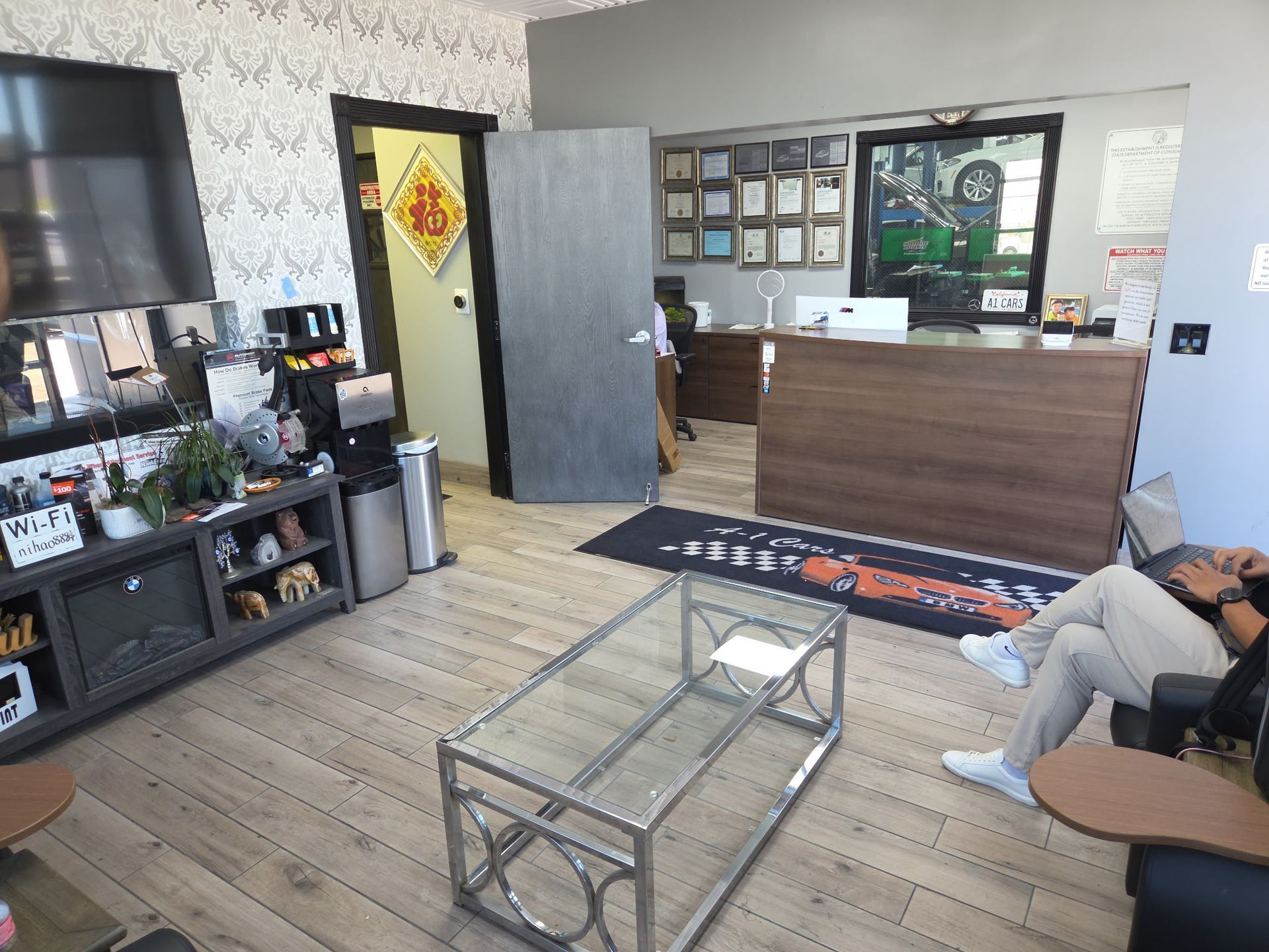 Lobby with a waiting area. A person sits in a chair. A reception desk and office are in the background.