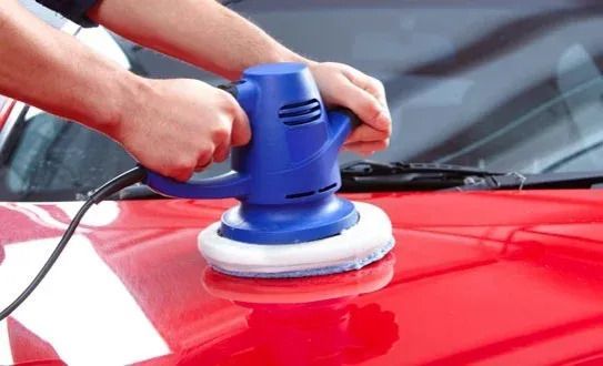 Person using a blue electric buffer to polish the red hood of a car.