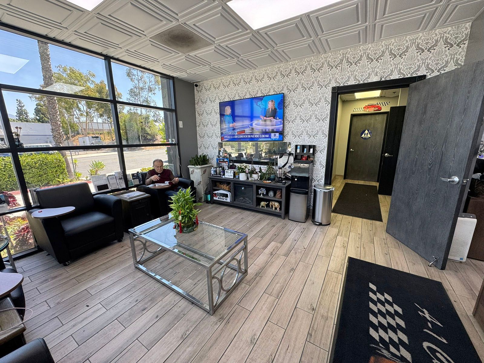 Modern office lobby with sofas, glass coffee table, TV, patterned walls, and hallway entrance