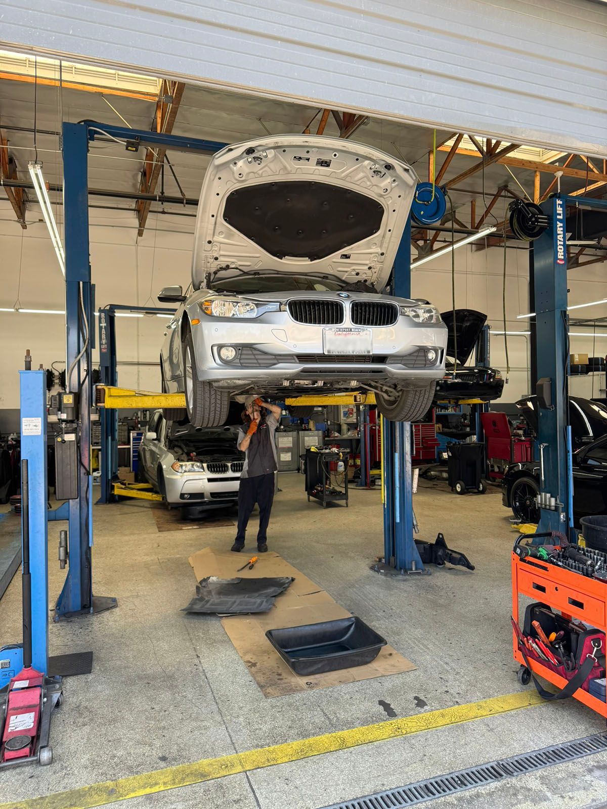 Car in a repair shop lifted on a hoist with hood open, mechanic standing underneath