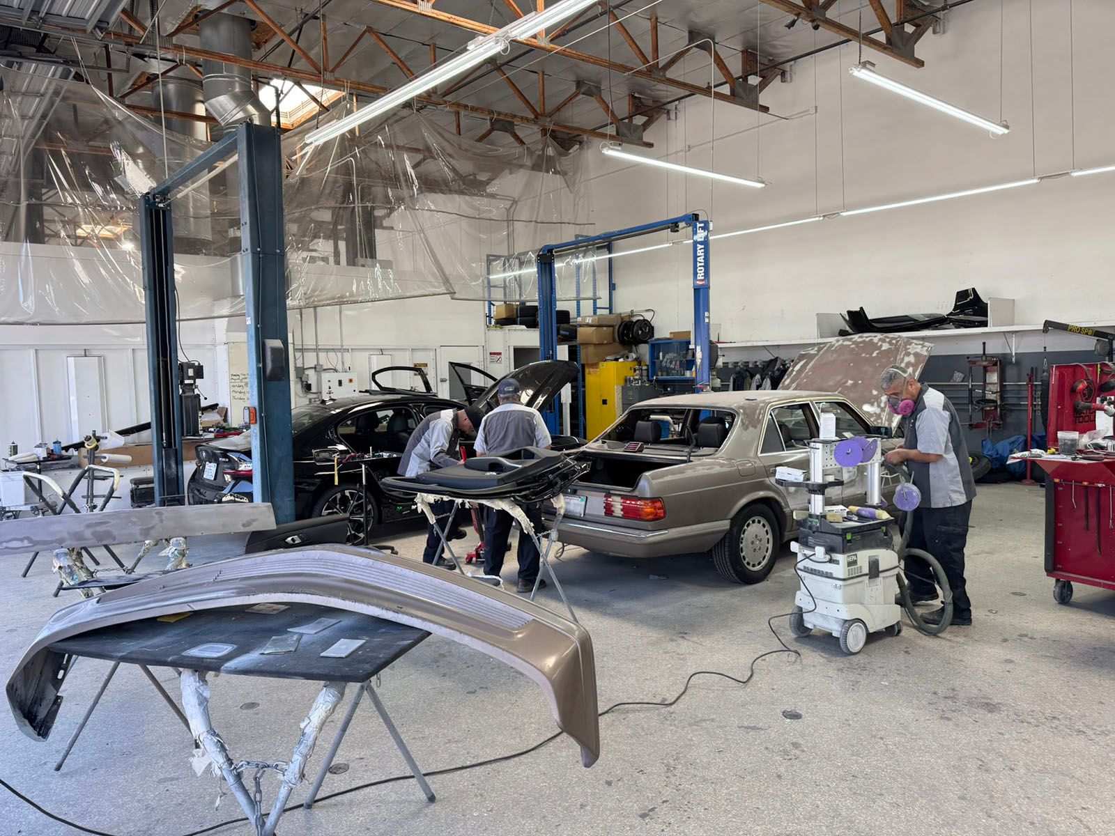 Auto repair shop with several cars, a lifted vehicle, and auto parts in a large industrial garage