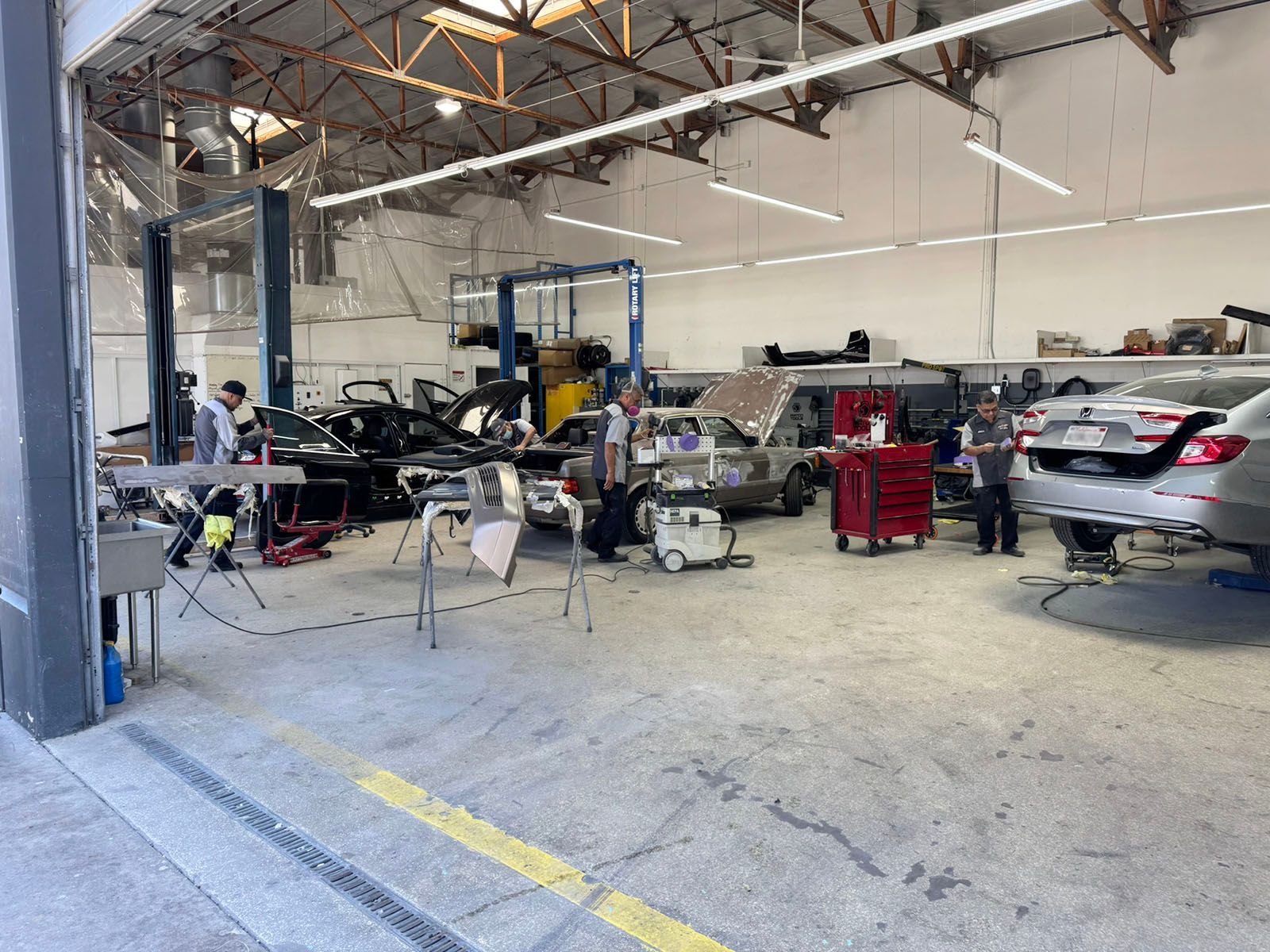 Auto repair shop interior with lifted cars, tools, and mechanics working under a high ceiling