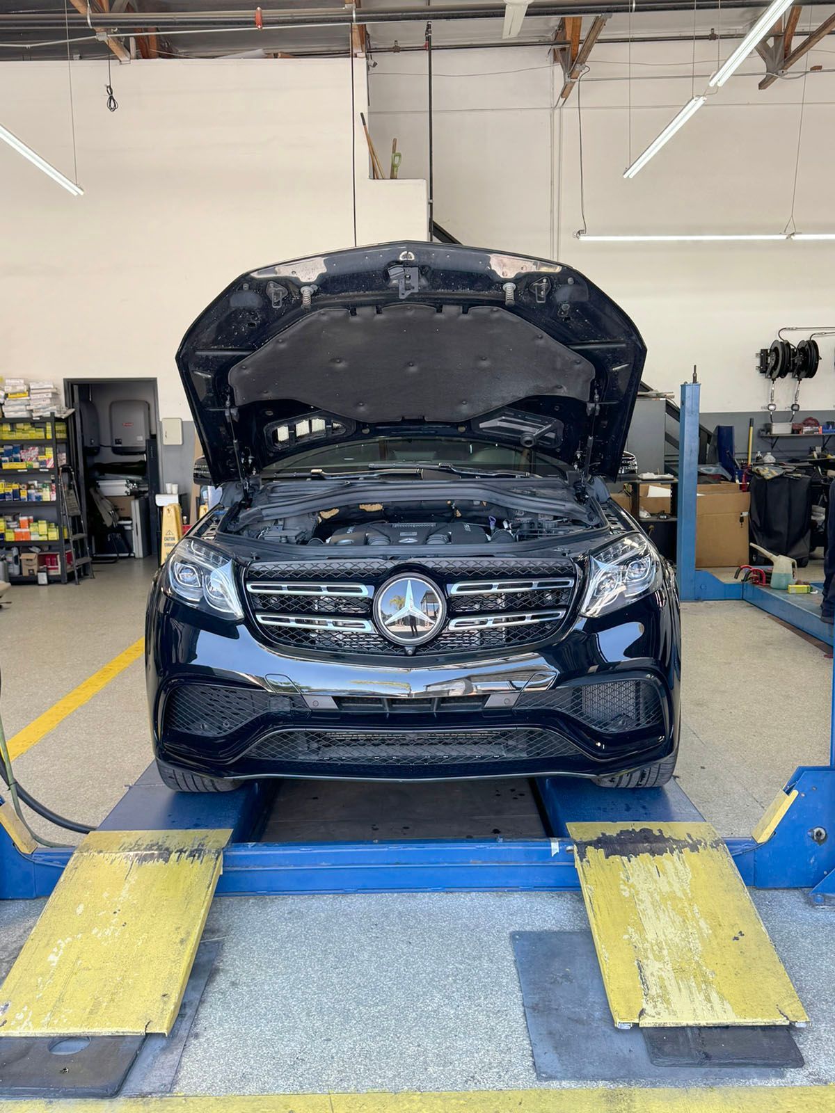Black car with hood open on a lift in an auto repair shop