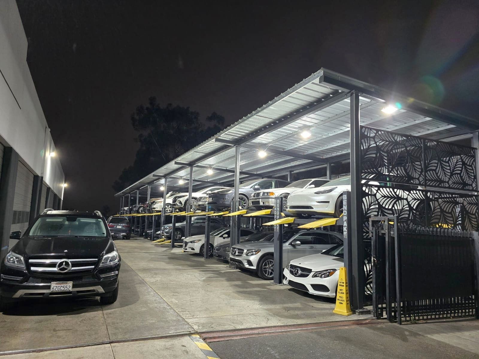 Covered car parking lot at night with several parked cars and bright overhead lights